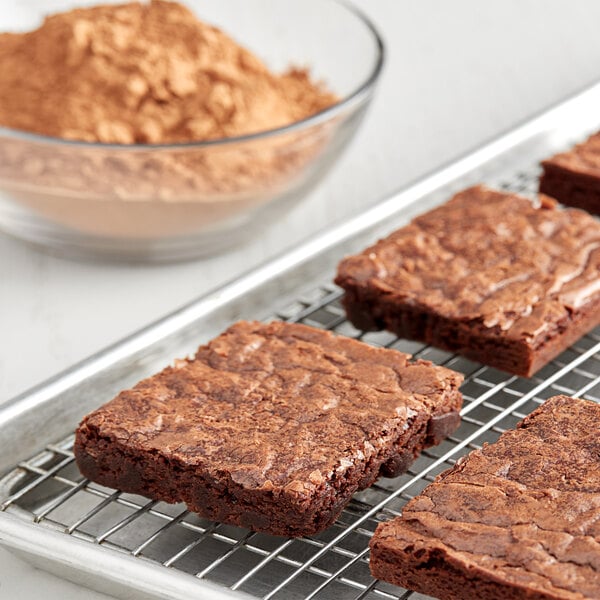A brownie on a cooling rack with a bowl of HERSHEY'S cocoa powder.