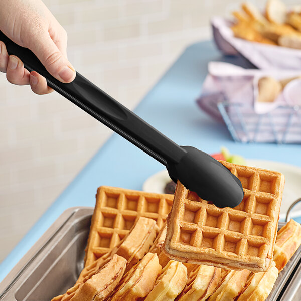 A hand holding a black Cambro scallop grip tong over waffles.