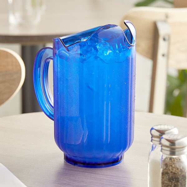 A Vollrath Traex Tuffex cobalt blue plastic pitcher on a table with ice and liquid.