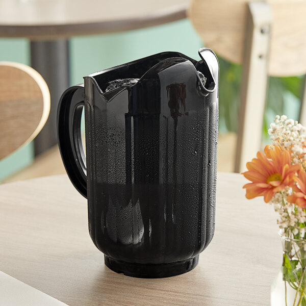 A black Vollrath Traex plastic pitcher on a table with flowers.