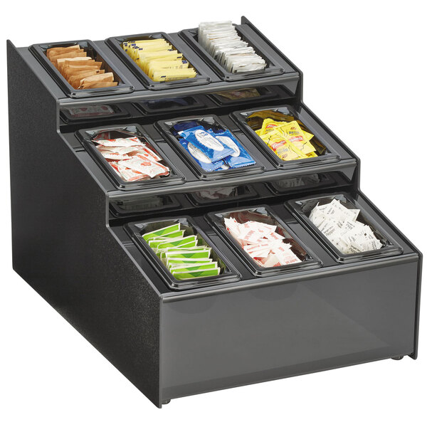 A black Vollrath 3 tier condiment organizer on a hotel buffet counter filled with different types of condiments.
