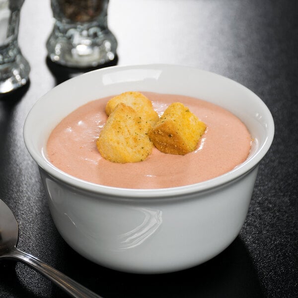 A white Cambro porcelain bowl filled with soup and croutons with a spoon next to it.