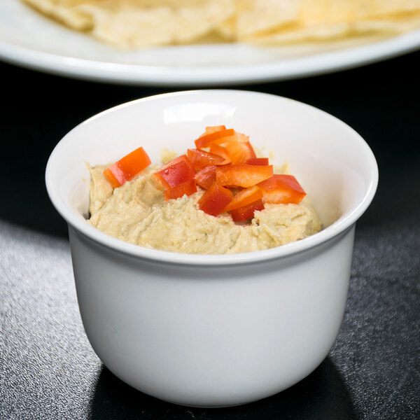 A white Cambro porcelain bowl filled with hummus and surrounded by red and orange food.