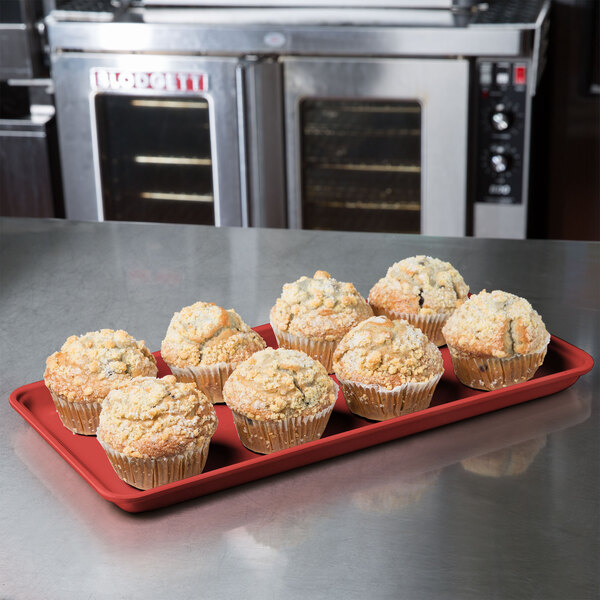 A red MFG Fiberglass Supreme Display Tray holding muffins on a counter.