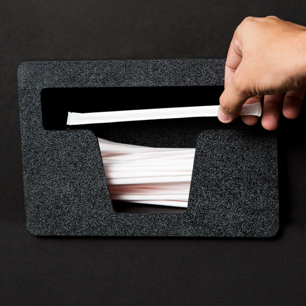 A hand holding a straw in a black Vollrath straw dispenser.