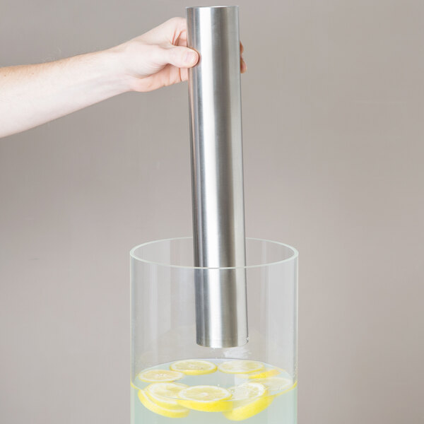 A hand using a Cal-Mil stainless steel metal tube to add lemon slices to a glass of water.