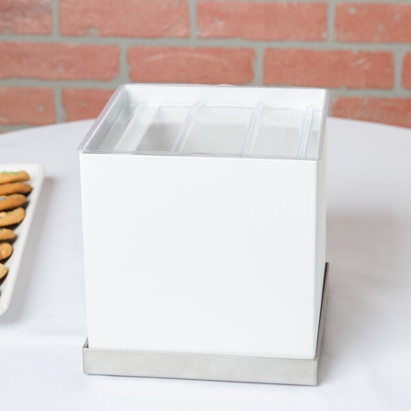 A white table with a Cal-Mil Luxe beverage dispenser base on top of a white box with a lid.