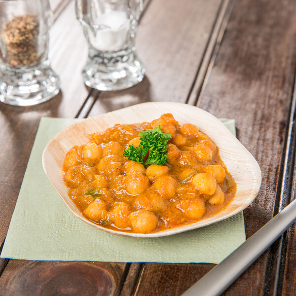 A bowl of food on a TreeVive palm leaf plate on a wood surface.
