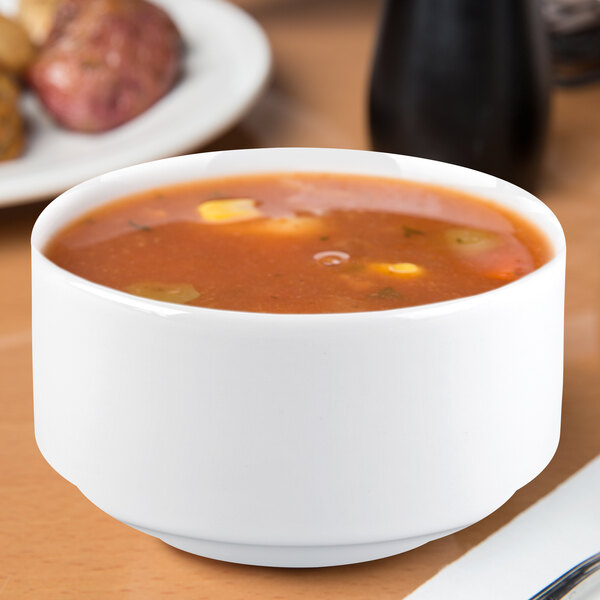 A stackable white Libbey porcelain bouillon cup filled with soup on a table.