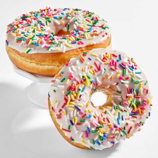A pair of donuts topped with white icing and colorful rainbow sprinkles.