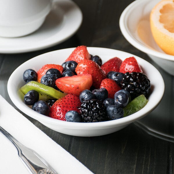 A Libbey white porcelain fruit bowl filled with fruit on a table.