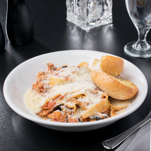 A Libbey white porcelain shallow bowl filled with pasta and bread on a table.