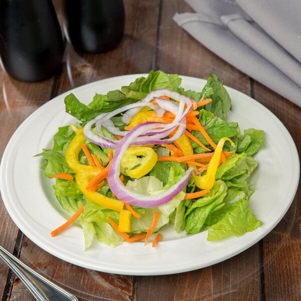 A Libbey ivory porcelain plate with a salad of vegetables and onions on it.