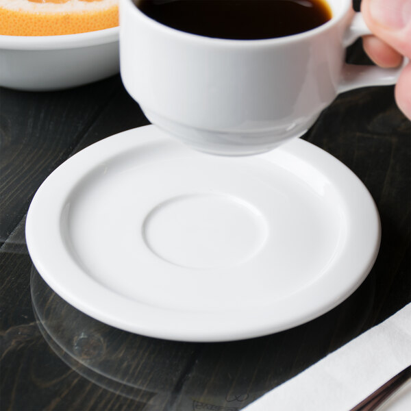 A hand holding a Libbey Reflections white porcelain tea saucer with a cup of coffee on it.