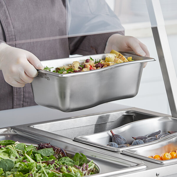 A person holding a Vollrath stainless steel pan with food in it.