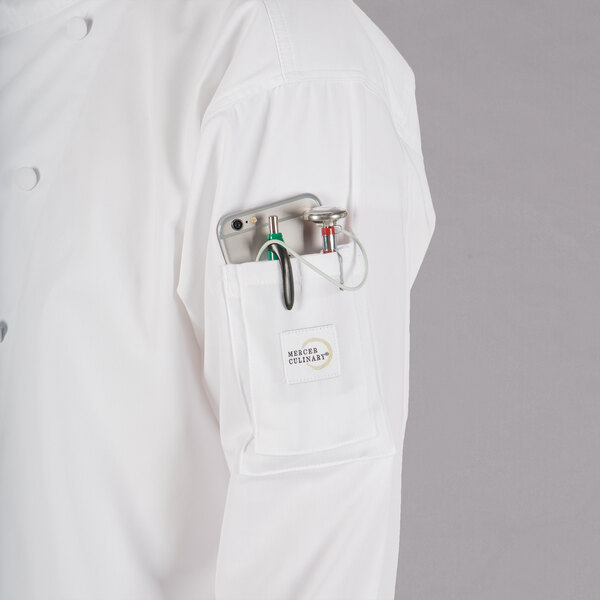 A person wearing a Mercer Culinary white chef jacket with a phone in the pocket.