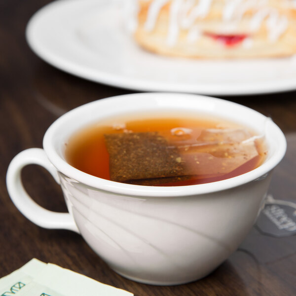 A Libbey ivory flint porcelain low tea cup filled with tea on a table with a pastry.