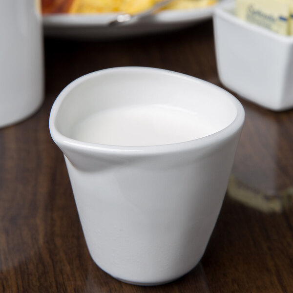 A white Libbey porcelain creamer with a liquid in it.