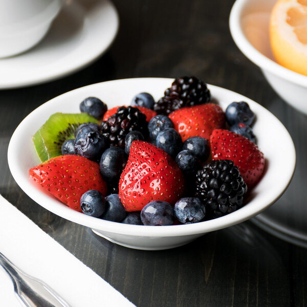 A Libbey white porcelain fruit bowl on a table with a bowl of fruit.