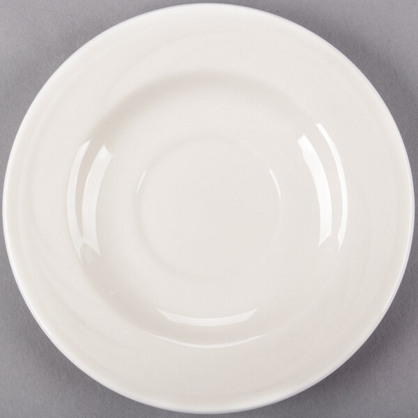 A Libbey ivory porcelain tea saucer with a rim on a gray surface.