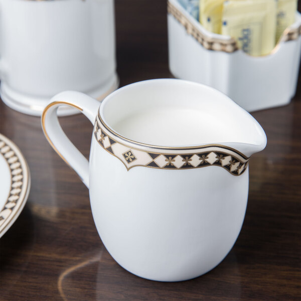 A white and gold Syracuse China Baroque creamer on a wood surface.