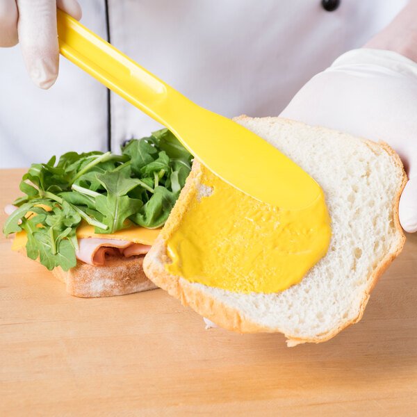 A person holding a yellow HS Inc. sandwich spreader over a sandwich.