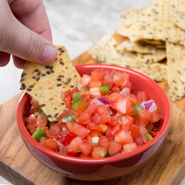 A hand holding a chip and dipping it into a bowl of salsa.