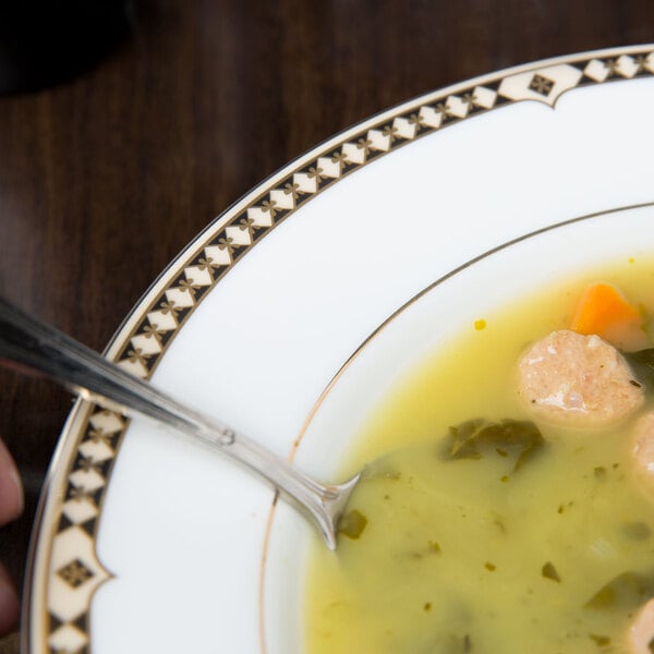A hand holding a spoon in a Syracuse China Baroque bone china soup bowl filled with sausage and vegetable soup.