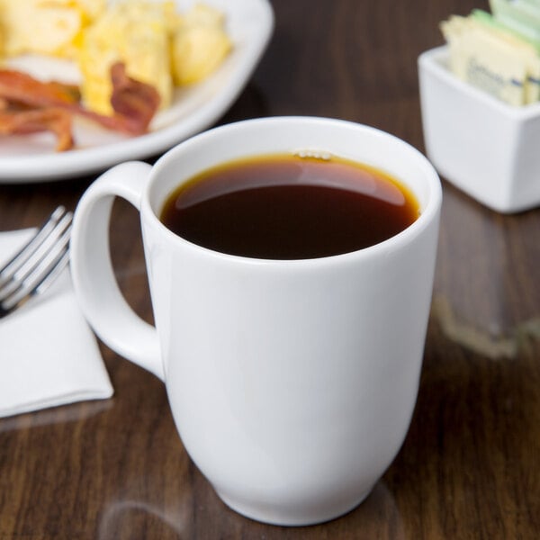 A white Libbey tall mug filled with brown coffee on a table with a plate of food.