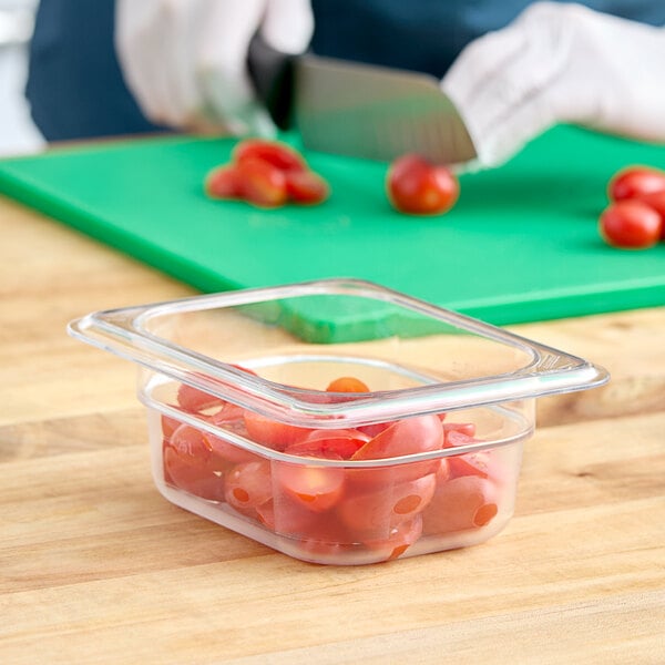A clear plastic Cambro food pan filled with tomatoes on a cutting board.