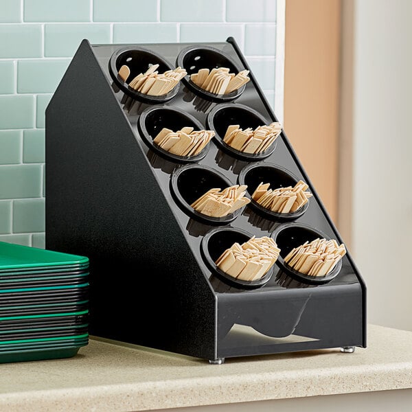 A black Vollrath countertop flatware organizer with black perforated cylinders holding wooden sticks.