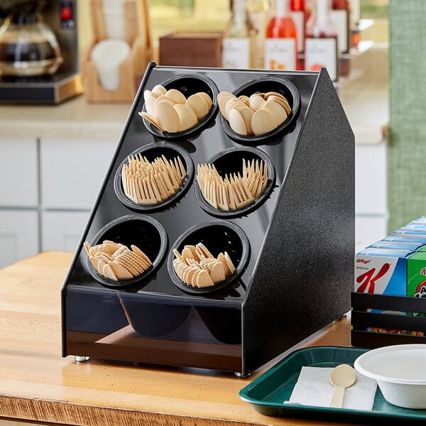 A black Vollrath countertop organizer with black and white flatware cylinders holding spoons and forks.