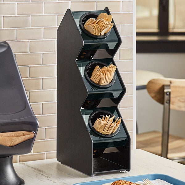 A black rectangular Vollrath countertop organizer with black cylinders holding utensils.