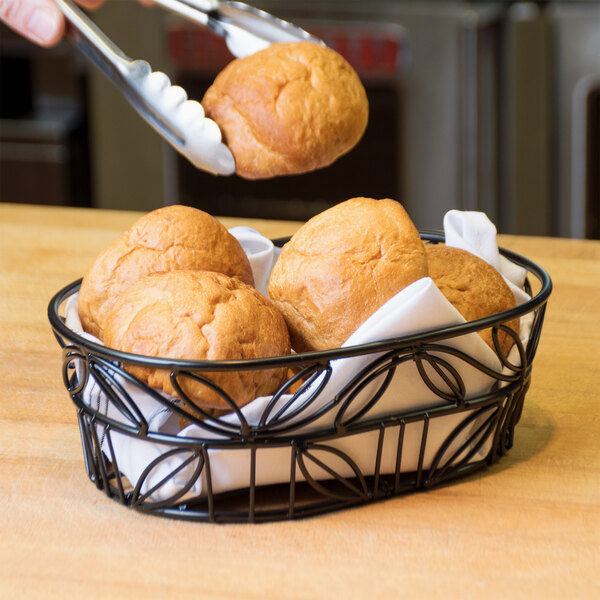 An American Metalcraft wrought iron oval basket with a leaf design holding rolls.