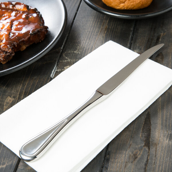 A Libbey stainless steel steak knife on a napkin next to a plate of food.