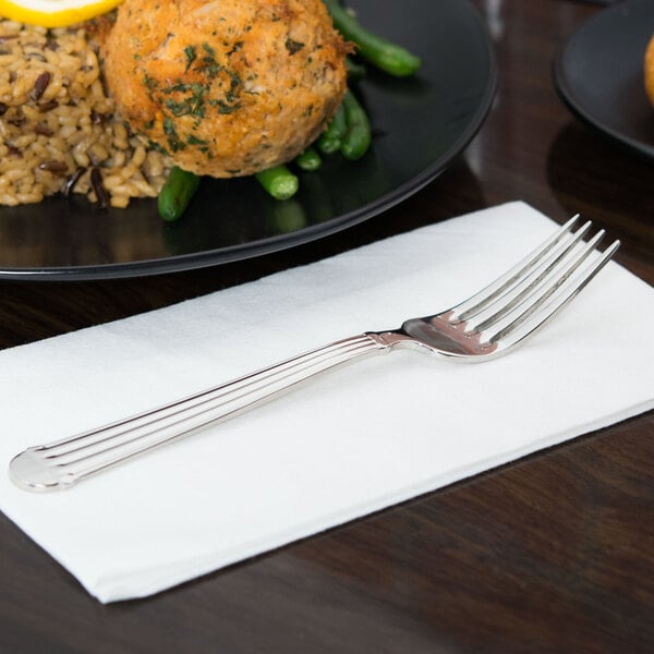 A stainless steel Libbey Aegean dessert fork on a white napkin next to a plate of food.