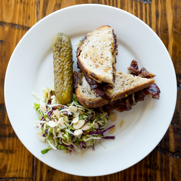 A 10 Strawberry Street Bistro porcelain dinner plate with a sandwich on it on a wood table.
