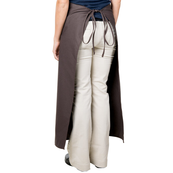 A woman wearing a brown Intedge bistro apron with 2 pockets over white pants.