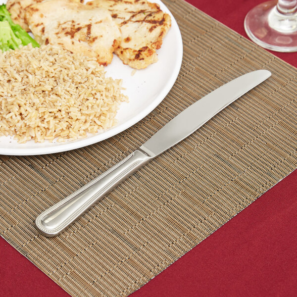 A plate of rice and vegetables on a place mat with a Libbey Calais stainless steel dinner knife.