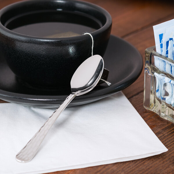 A black cup of tea with a Libbey stainless steel demitasse spoon on a saucer.