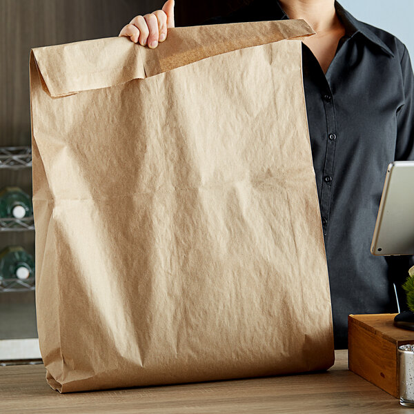 A woman holding a Duro brown paper merchandise bag with a pizza on a counter.