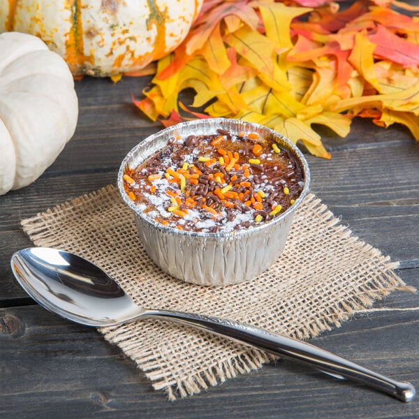 A small cup of dessert with a World Tableware stainless steel dessert spoon and brown and orange sprinkles.