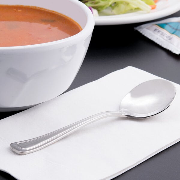 A bowl of soup on a napkin with a Libbey stainless steel bouillon spoon.