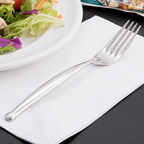 A World Tableware stainless steel salad fork on a napkin next to a plate of salad.