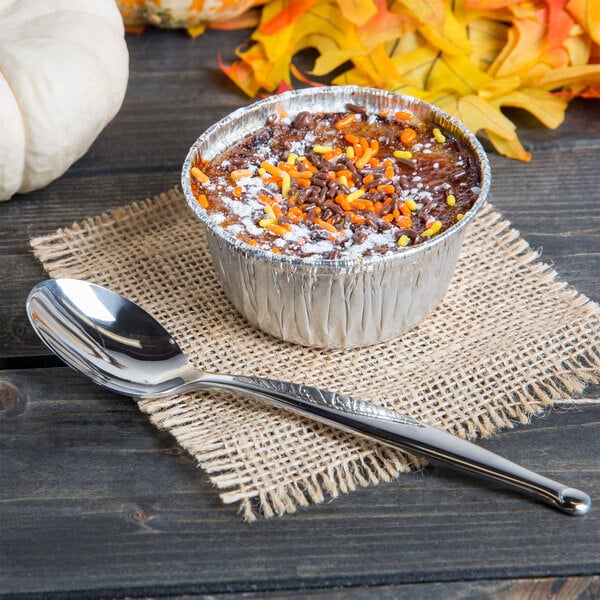 A cup of dessert with sprinkles and a World Tableware stainless steel teaspoon on a burlap cloth.