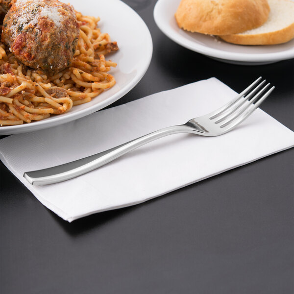 A Libbey stainless steel dinner fork on a napkin next to a plate of spaghetti and meatballs.