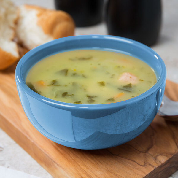 A Libbey blueberry porcelain bouillon filled with soup on a wood surface.