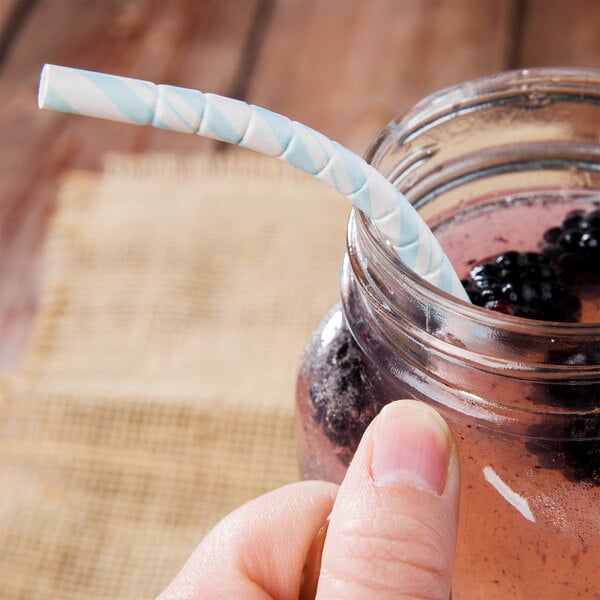 A person holding a Creative Converting pastel blue and white striped paper straw in a jar of liquid.