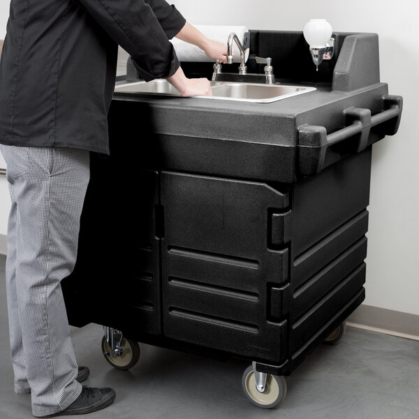 A man standing next to a black Cambro portable hand sink on a counter.