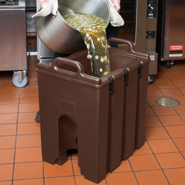 A man pouring liquid into a dark brown Cambro soup carrier.